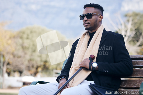 Image of Blind black man, park bench and outdoor with sunglasses, walking stick or relax by trees, peace or thinking. African guy, vintage fashion and young person with disability, glasses or travel in nature