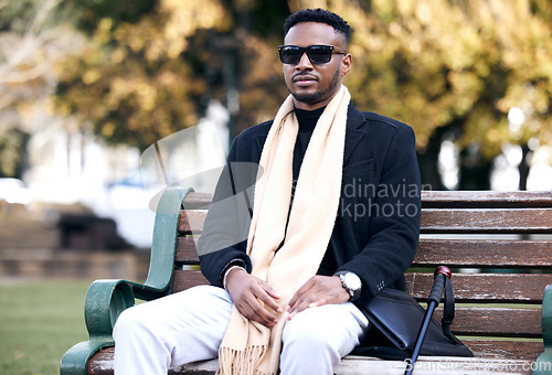 Image of Blind black man, park bench and relax with sunglasses, walking stick or outdoor by trees, peace or thinking. African guy, vintage fashion and young person with disability, glasses or travel in nature