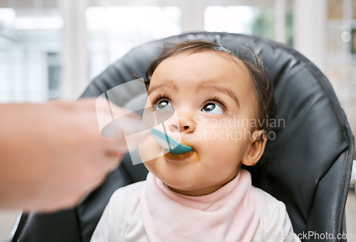Image of Adorable, sweet and cute baby eating puree for lunch, dinner or snack in her high chair at home. Child development, food and girl infant kid enjoying meal with spoon for growth and wellness in house.