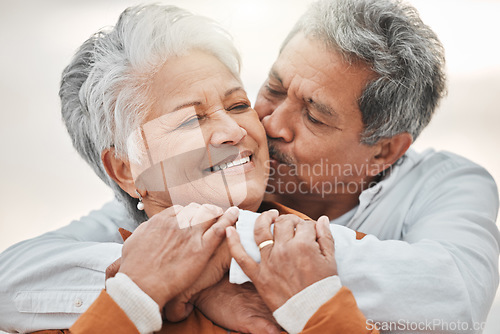 Image of Happy elderly couple, hug and sunset with kiss on cheek, bonding and smile for romance, love and vacation. Senior man, woman and embrace with happiness, retirement and travel together for holiday