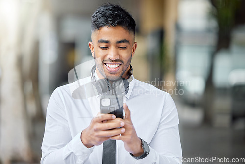 Image of Business man, phone text and city of a professional with headphones watching a video. Urban, smile and Indian male person with work travel, mobile streaming and happiness with cellphone app and web