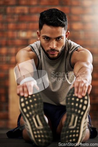 Image of Gym, feet and portrait of man stretching, workout warm up and motivation for fitness mindset. Focus, commitment and face of athlete on floor, stretch and training legs at sports club for health goals