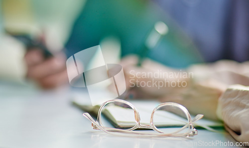 Image of Glasses on desk, vision and eye care with business people in meeting, writing in notebook with strategy collaboration closeup. Eyewear, prescription lens and notes with ideas, planning with team