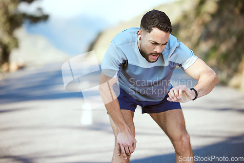 Image of Man, fitness and outdoor with a watch for a run or exercise with performance progress. Tired athlete person or runner on a road with time and music for training, running or health and wellness goals