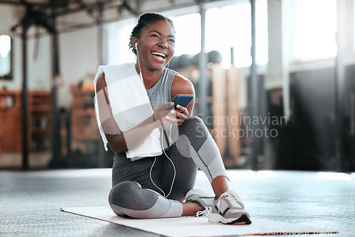 Image of Phone, earphones and funny black woman in gym for fitness, sports or exercise. Smartphone, music and African female athlete laughing at web meme or comedy on break after workout, training or pilates.