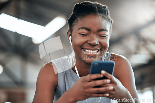 Image of Phone, earphones and happy black woman in gym for fitness, sports or exercise. Smartphone, music and African female athlete on social media break, internet and web texting after workout or training.