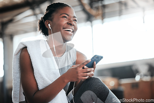 Image of Earphones, smartphone and laughing black woman in gym for fitness, sports or exercise. Phone, music or African female athlete laugh at funny meme or comedy on break after workout, training or pilates