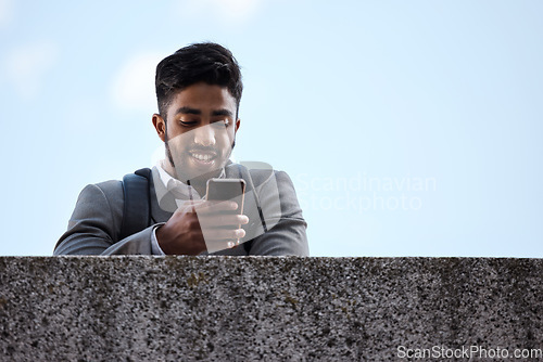 Image of Phone, networking and businessman by a wall in the city browsing on social media or mobile app. Happy, smile and professional male employee scrolling on the internet while waiting for a cab in town.