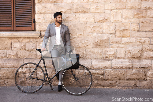 Image of Bicycle, suit and businessman in the city for travel standing by a brick wall building. Briefcase, professional and young male employee riding a bike or commuting to his work office in an urban town.