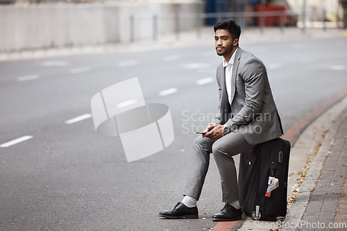 Image of Suitcase, road and businessman in the city for travel to airport for corporate company trip. Phone, bag and professional male employee sitting in urban town road waiting for a cab, taxi or transport.