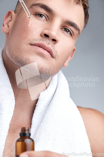 Image of Skincare, oil and man with serum, dermatology and natural beauty against a grey studio background. Face, male person or model with cosmetics, wellness and spa treatment with grooming routine and glow