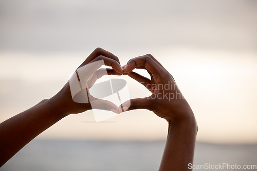 Image of Hand, heart and love sign at the beach with romantic, emoji and happiness hands gesture. Outdoor, sea and ocean with person holding romance, loving and valentines sign on holiday in nature at sunset