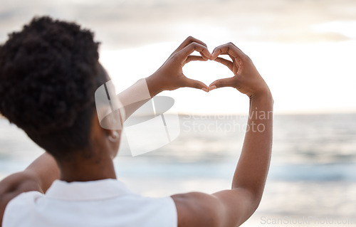 Image of Woman hand, heart and love sign at the beach with romantic, emoji and happiness hands gesture. Outdoor, sea and ocean with female person back with kindness sign on holiday in nature at sunset