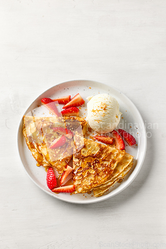 Image of crepes decorated with honey, strawberries and ice cream