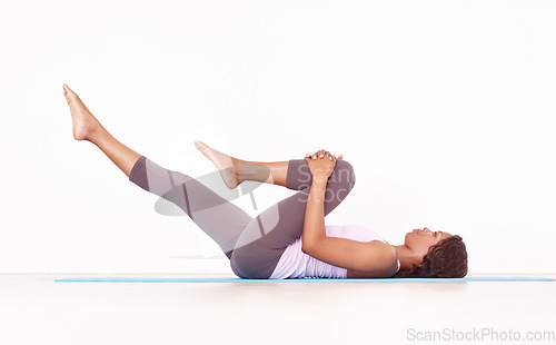 Image of Yoga, leg stretch and black woman in studio on a fitness and workout mat for training. Isolated, white background and African female person lying on the ground with sport stretching for wellness