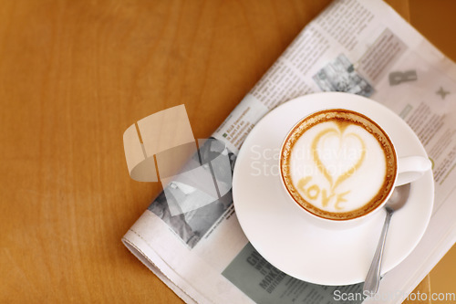 Image of Coffee, cappuccino and heart in foam with newspaper on a table with no people in a restaurant. Cafe drink, love writing and foamy beverage art with milk in a cafe with a closeup of mug and mockup