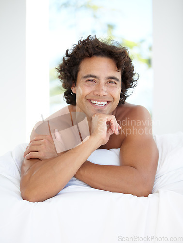 Image of Portrait, smile and bedroom with a man lying on a bed in his home to relax or rest on a summer morning. Happy, wellness and lifestyle with an attractive young male person relaxing alone in his house
