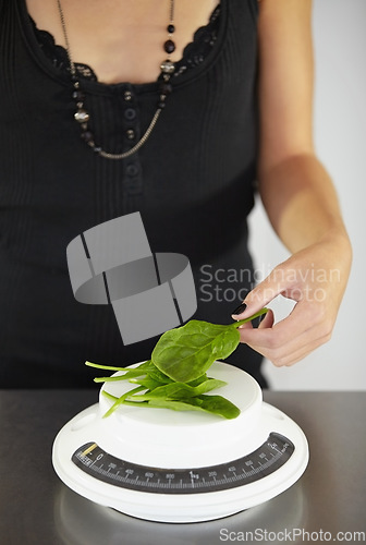 Image of Hand, scale and spinach in kitchen for diet, food or eating disorder with leaves for meal plan. Woman, mental health and vegetable leaf to lose weight with anorexia, bulimia or starving in home