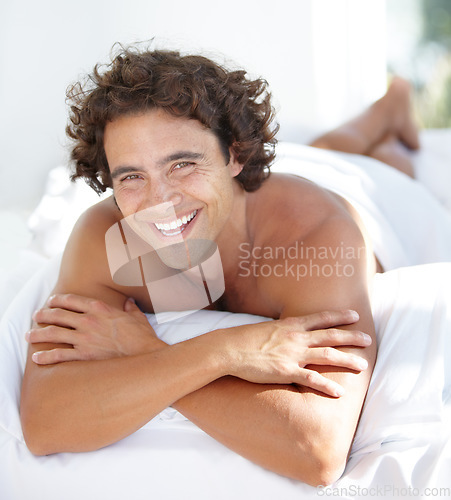 Image of Portrait, happy and bedroom with a man lying on a bed in his home to relax or rest on a summer morning. Smile, wellness and lifestyle with an attractive young male person relaxing alone in his house