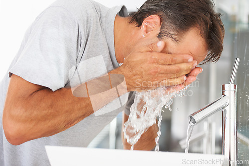 Image of Hygiene, hydration and a man washing his face in the bathroom of his home in the morning to wake up. Fresh, water and cleaning with a male person in his house to start a skincare or moisture routine