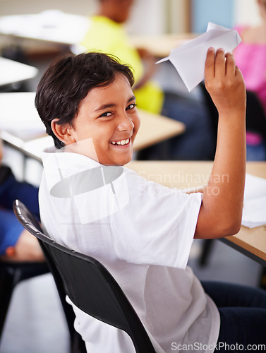 Image of Portrait, student and paper plane in classroom and happy, learning at desks or Indian boy, play and origami jet or class distraction. Playful smile, kid and holding airplane and middle school fun