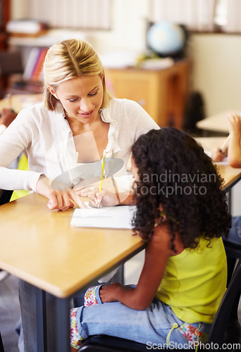 Image of Teaching, writing and teacher helping child at school with education, learning or development. Woman talking to girl student with notebook, pencil and knowledge at classroom desk with support