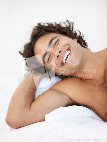 Image of Face, laugh and a handsome man in bed in his home to relax or rest alone on a summer morning. Smile, wellness and lifestyle with a happy young male person relaxing in the bedroom of his house