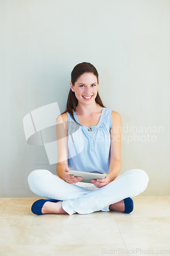 Image of Portrait, tablet and a woman sitting legs crossed on the floor of her home browsing social media with a smile. Happy, technology and app with a young female person using the internet against a wall