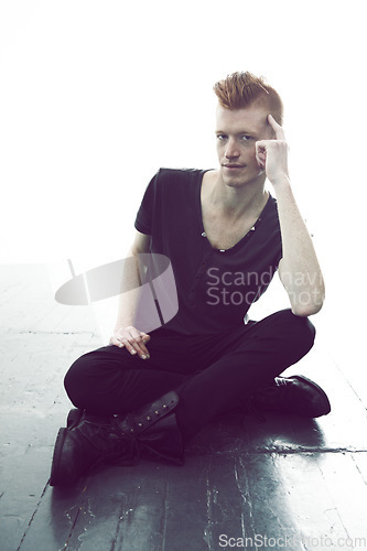 Image of Portrait, ginger and man sitting on a floor with hand on head or wearing black or in thought for fashion and against white wall. Mohawk, dark and young guy thinking in punk clothes or rock and roll