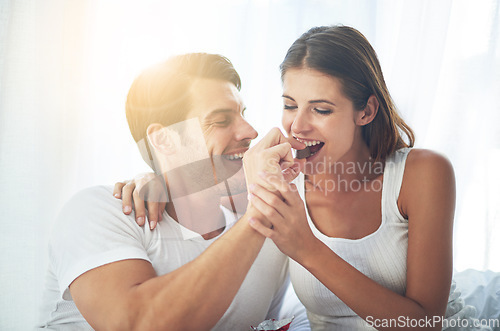 Image of Love, happy couple eat chocolate in bedroom and care with smiling or laughing. Valentines day, married people sharing sweet snack and spending quality time in their home and romance or caring