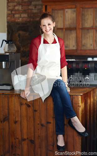Image of Woman in portrait, barista at coffee shop and sit on countertop, happy employee in hospitality industry. Female professional in cafe, small business owner and entrepreneur smile with positive mindset