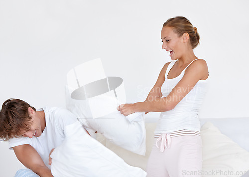 Image of Happy, fun and couple in a pillow fight on the bed in the hotel room on a romantic weekend trip. Happiness, laughing and young woman and man playing together in the morning in the bedroom at home.