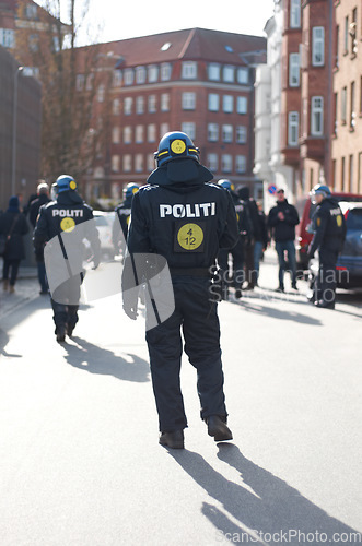 Image of Security, justice and back of policeman in the city working to patrol protest or march. Law enforcement, public service and safety guard or officer in uniform for protection in town street in Denmark