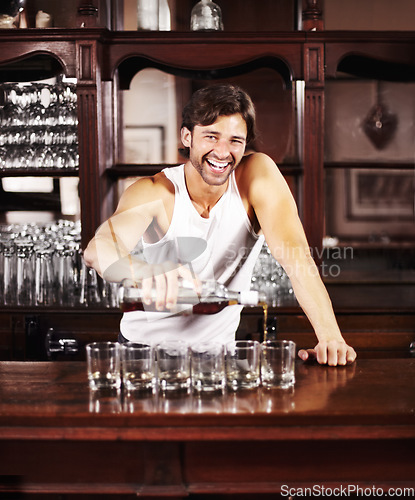 Image of Portrait, whisky and alcohol with a handsome barman behind the counter of a pub to serve drinks during happy hour. Smile, glass and drink with a man bartender pouring a whiskey beverage in a bar