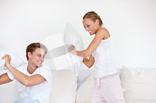 Image of Love, pillow fight and couple being playful on the bed in the hotel room on a romantic weekend trip. Happiness, laughing and young woman and man playing together in the morning in the bedroom at home