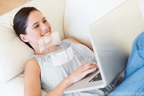 Image of Relax, happy woman and laptop on a sofa streaming, social media and reading in her home. Lying down, smile and female online in a living room with subscription, entertainment and internet search