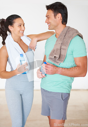 Image of Man, woman and chat in gym with smile, break and relax together after workout for fitness, health and wellness. Happy couple of friends, talking and drinking water for training, exercise or lifestyle