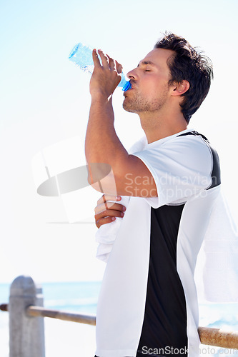 Image of Man, fitness and drinking water for hydration, health or wellness after workout, exercise or training at the beach. Fit, active and thirsty male having a drink in break or refreshment from exercising