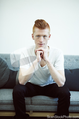 Image of Serious, couch and portrait of man with ginger hair or sit in a lounge in thought or for hipster fashion and against white wall. Sofa, think and young person with funky, casual style or relax at home