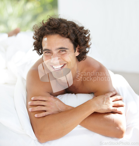 Image of Portrait, happy and relax with a man on a bed in his home, lying in the bedroom to rest on a summer morning. Smile, wellness and lifestyle with an attractive young male person relaxing in his house