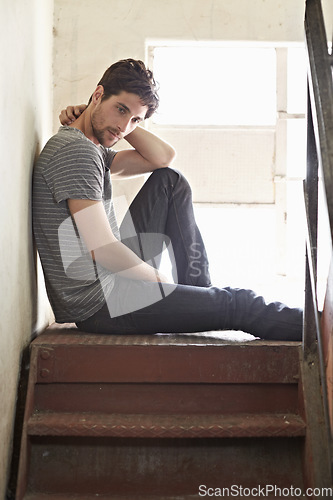 Image of Thinking, depression and lonely with a man on a staircase in his home, sitting on the landing by a window. Idea, mental health and relax with a handsome young male on steps or stairs in his house