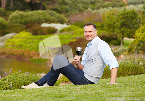 Image of Mature man with red wine outdoor, relax with smile in nature with alcohol drink, leisure and travel to countryside. Happy male person with alcoholic beverage in glass, satisfied and relaxing in park