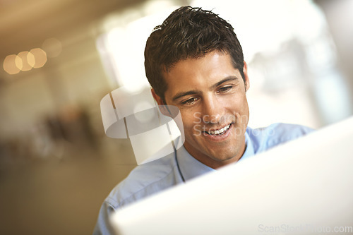 Image of Computer, face and blurred background with a business man at work on a project in his office. Smile, internet and technology with a young male employee working on a desktop for a company report