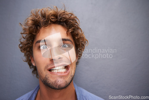 Image of Young man, portrait and silly face for funny or goofy expression against a gray wall background. Male with crazy humor or impression looking and posing in playful happiness or fun manner and attitude