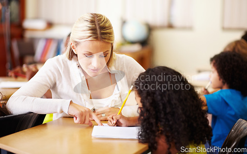 Image of Teacher, teaching and child learning to write at school for education, knowledge or development. Woman with girl student for solution, notebook and pencil at a classroom desk with support and help