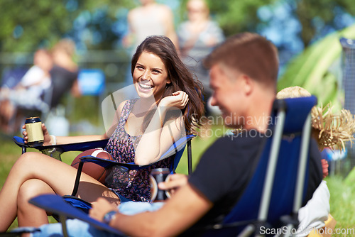 Image of Portrait, woman drinking a beer at music festival or camping site and smiling with her friend. Vacation, happy female person sitting on camp chair and having a beverage while talking to her a male