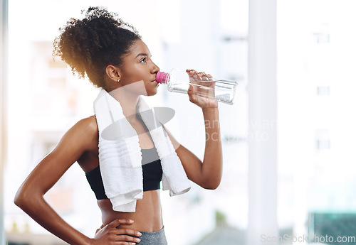 Image of Fitness, young woman athlete and water or bottle for exercise hydration or after workout with towel and in gym. Bodybuilding, training and wellness or girl runner drink or detox sweat and healthy