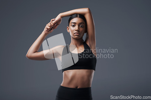 Image of Portrait, mockup space and stretching with a woman in studio on a gray background for exercise or health. Fitness, workout and warm up with an attractive young female athlete training her body