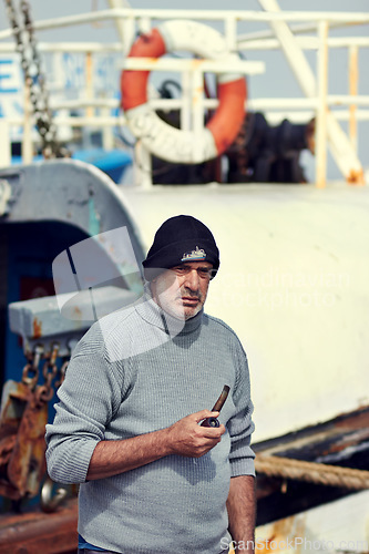 Image of Fisherman boat, mature man portrait and smoking pipe by the sea water at a port for fishing. Old man, ocean and senior dock worker sitting by boats outdoor with tobacco smoke at a harbor for work