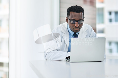 Image of Healthcare, research and man doctor on laptop in consultation office for reading in hospital. Online, medical and African male health expert checking medical news, development or clinic schedule